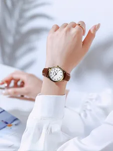 Elegant women's quartz watch with brown leather strap and gold bezel on a white desk