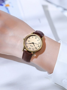 Close-up of minimalist women quartz watch with gold round case and dark brown leather strap