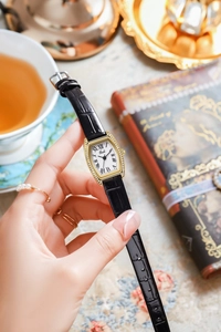 Detail of tonneau gold watch with crystal bezel and black Roman numerals on white dial