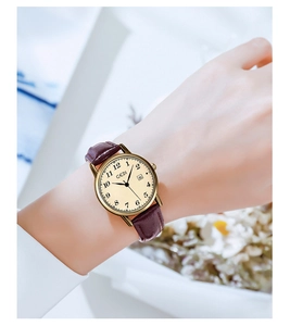 Close-up of vintage gold ladies watch with cream dial and brown leather strap on wrist