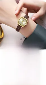 Detail of vintage octagonal gold watch with brown leather strap worn on wrist