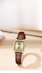 Dettaglio di un orologio quadrato dorato vintage con cinturino in pelle marrone su tavolo