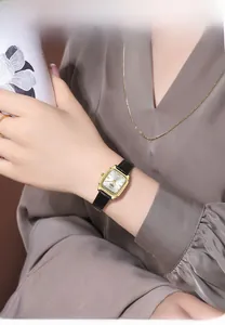 Dettaglio dell'orologio rettangolare dorato con cinturino in pelle nera sul polso