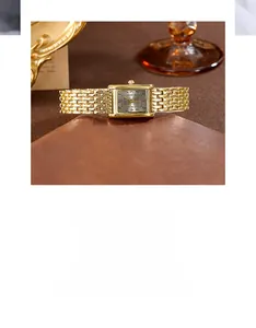 Detail view of a vintage square gold watch with a metallic chain bracelet on a desk
