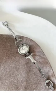 Macro shot of silver oval minimalist watch dial and slim bangle strap on soft knit fabric