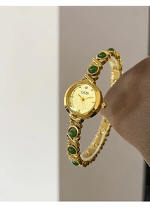 Detail of GEDI gold bracelet watch with green gemstone links and elegant polished metal dial