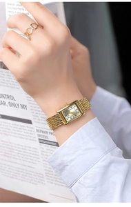Detail of elegant gold rectangular watch with mesh strap and triple heart ring on wrist