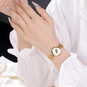 Détail d'une montre bracelet dorée à maillons en cœur avec manche en dentelle