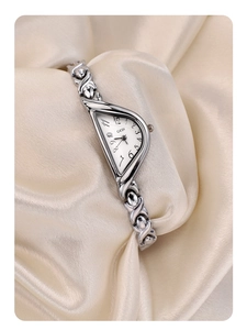 Detailed shot of silver-tone irregular crescent watch with chain strap on silk fabric
