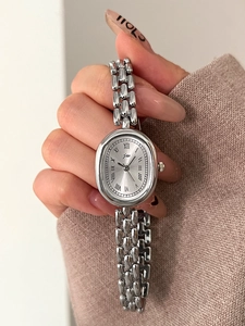 Detailed close-up of a silver oval quartz watch with roman numerals on a link bracelet