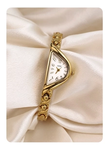 Detailed shot of vintage gold quartz watch with triangle dial on silk background