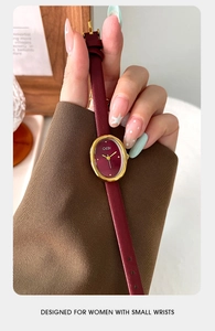 Close-up of vintage oval gold watch with burgundy dial and red leather strap