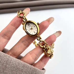 Detail of GEDI gold oval watch featuring a crystal-set bee charm and chain bracelet