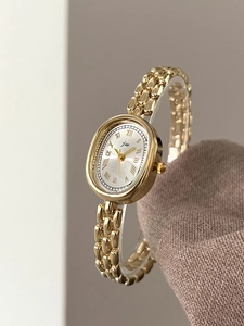Close-up of golden oval watch with silver Roman dial and polished chain strap