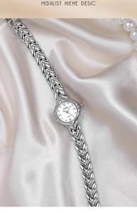 Detail of silver leaf-shaped bracelet watch with white dial on champagne silk background