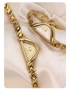 Close-up of GEDI gold crescent watches with X-shaped metal straps on silk fabric
