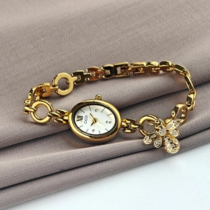Gedi gold oval watch with rhinestone butterfly charm on a gray fabric background