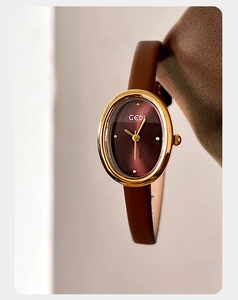 Macro detail of oval gold case and burgundy dial on vintage leather strap watch