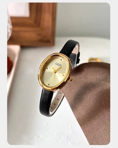 Detailed close-up of oval gold watch with minimalist dial and black leather strap