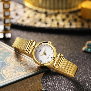 Montre quartz femme dorée avec bracelet en maille et cadran blanc sur un livre vintage