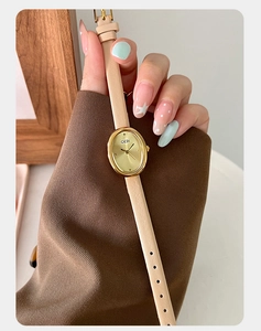 Close-up of small vintage oval watch with golden dial and beige leather strap on wrist