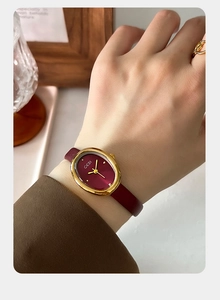 Close-up of elegant oval gold watch with burgundy dial and leather strap on a wrist