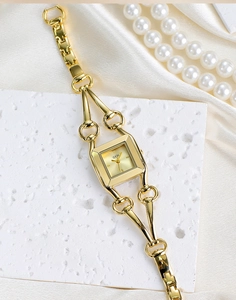 Detail of elegant gold square watch on white stone with decorative pearls and satin