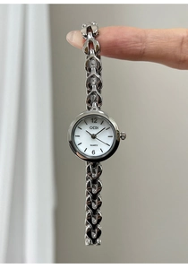 Vertikale Ansicht einer silbernen herzförmigen Kettenuhr, die an den Fingern hängt