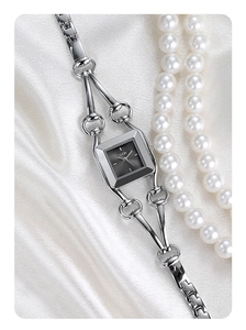 Detail of silver square quartz watch with horsebit chain strap on white silk background