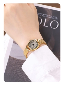 Close-up of gold tonneau watch with roman numerals and metallic expansion strap