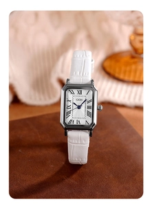 Macro shot of a rectangular silver watch with white crocodile leather strap on brown base