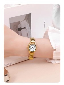 Close-up of golden tonneau watch on female wrist with Roman numeral dial and steel strap