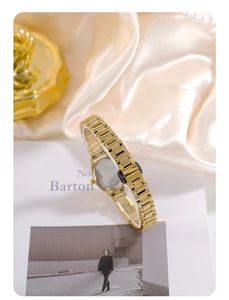 Close-up of elegant gold tonneau watch with metal mesh strap on creamy silk fabric