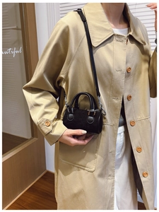 Détail d'un mini sac seau noir en velours côtelé porté avec un trench-coat kaki élégant