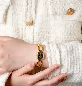 Detail of elegant gold chain watch with square black dial worn on wrist over tweed