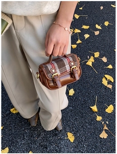 Outdoor shot of vintage plaid wool handbag with golden buckles on ginkgo leaf background