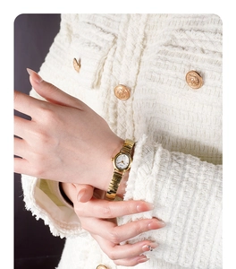 Detail view of a luxury gold women's watch with elastic band worn with a tweed jacket