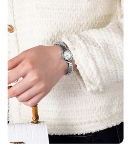 Detail of silver ladies watch with metal strap paired with a bamboo handle handbag