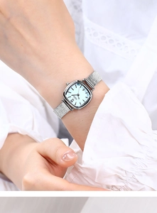 Close-up of a square silver quartz watch with a light blue dial and mesh strap