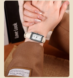 Detail of a rectangular silver quartz watch with a cream leather strap on a model wrist