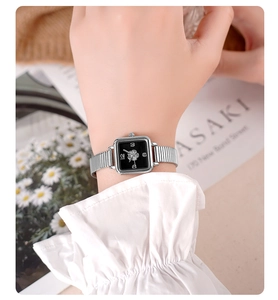 Detailed shot of a silver square watch with black dial and clover motif on a female wrist