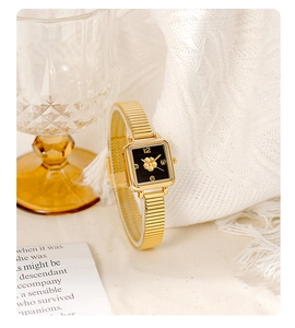 Detail of square gold watch with black dial and floral relief on white knit background