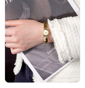 Close-up of elegant gold oval quartz watch styled on wrist with white textured clothing