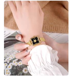 Close-up of vintage square gold watch with camellia flower motif on black dial