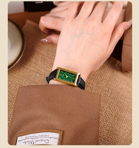 Close-up of a vintage rectangular gold watch with green dial on a woman's wrist