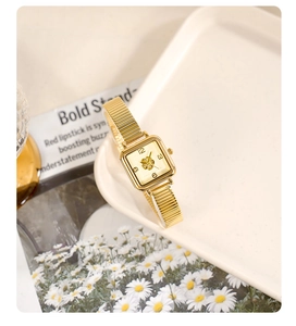 Detail of square gold watch with floral relief on dial and snake chain strap