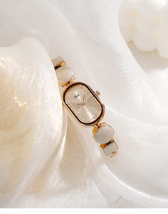 Detail of Gedi quartz watch with oval gold dial and pearl chain strap on white silk