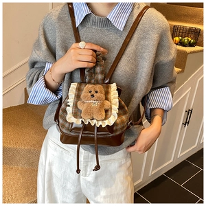 Dettaglio di uno zaino per bambini a quadri con pizzo e un simpatico orsetto di peluche