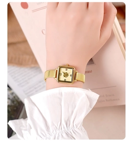 Close-up of golden square quartz watch with bamboo-style band on an elegant wrist