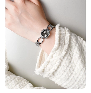Detail of silver chain bracelet watch with a rectangular dial worn on a tweed sleeve